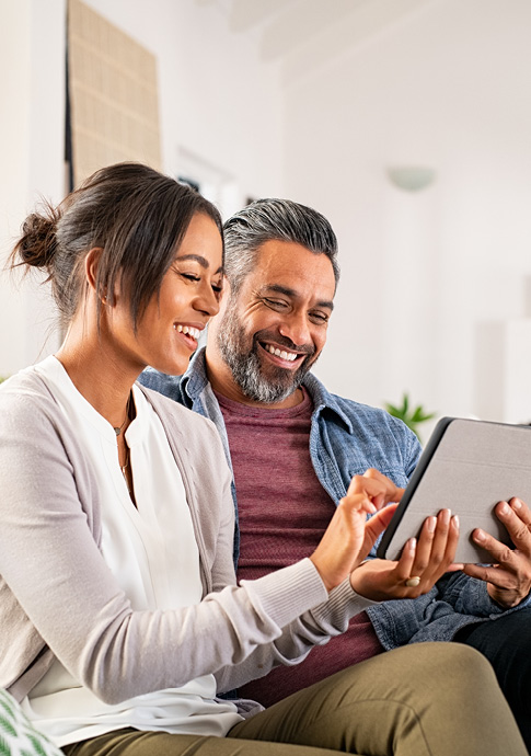 Man and woman sitting down smiling while using an iPad