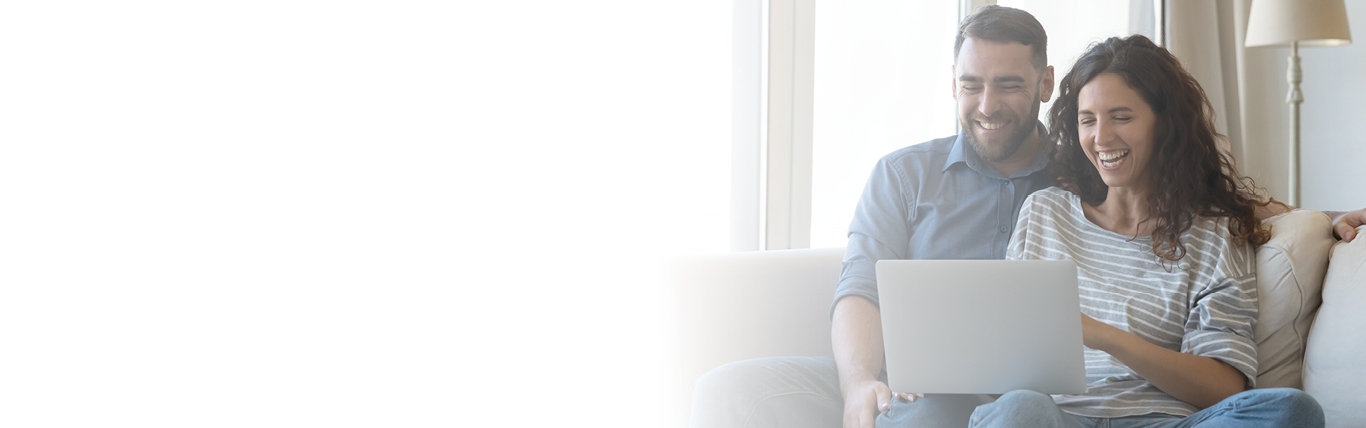couple smiling sitting on couch using a laptop
